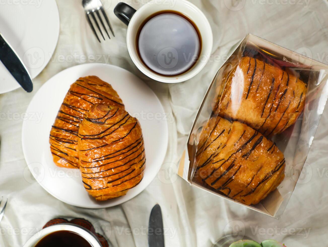 Chocolate Croissant served on plate with cup of black coffee with knife and fork isolated on napkin top view of french breakfast baked food item on grey background photo
