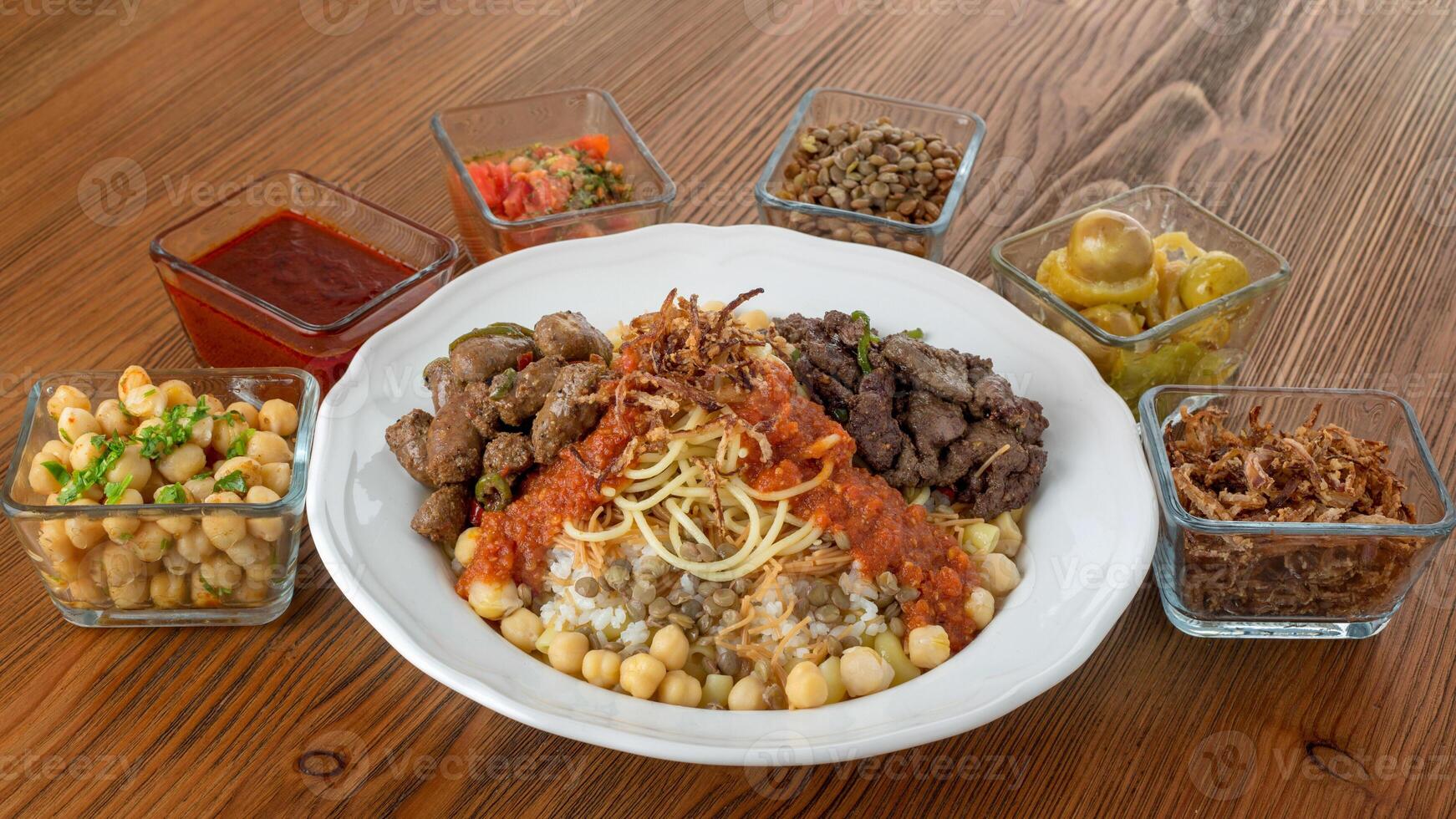 Koushari egyptian food with chicken liver and beef kebab, chickpea, noodles, boiled rice, lentil, fried onion, tomato, chili sauce and pickle served in dish isolated on table top view of arabic food photo