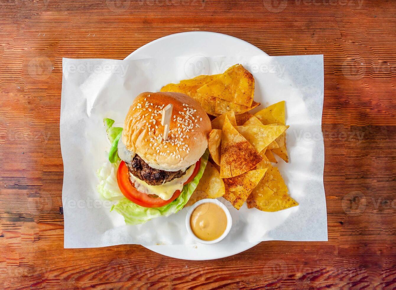 imposible hamburguesa con carne de vaca empanada, pepino, tomate y repollo, mayonesa inmersión y galletas servido en plato aislado en de madera mesa parte superior ver de hong kong comida foto