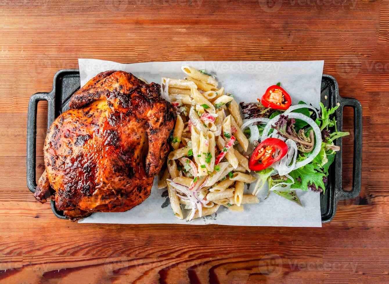 Whole grilled chicken with side dishes penne salad served on board isolated on wooden table top view of hong kong food photo