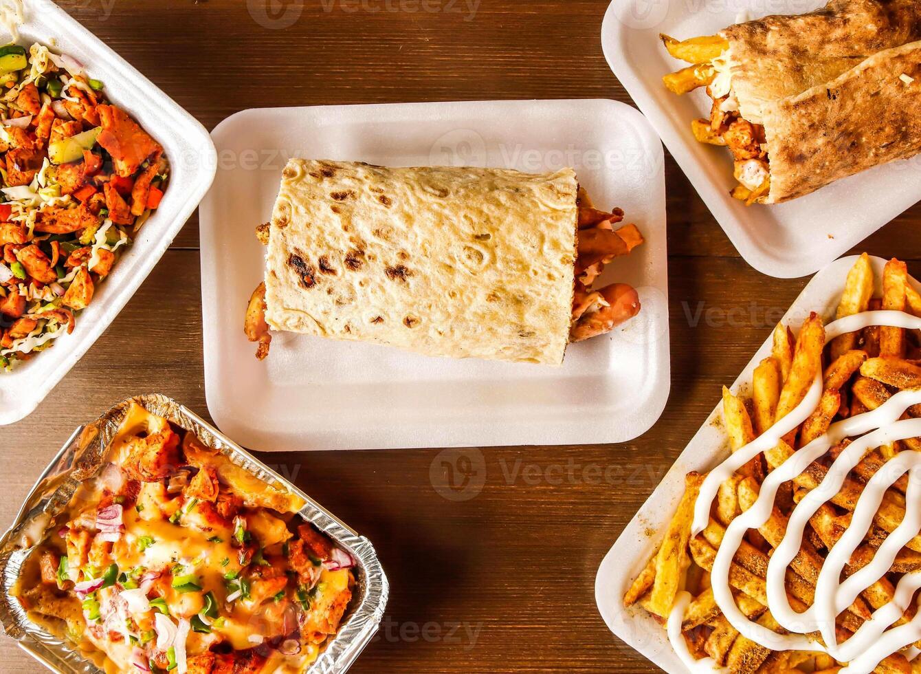 afghani sausage shawarma, chicken wrap, pizza loaded fries, mayo fries or potato chips and chicken diet salad served in dish isolated on wooden background top view of indian spices and pakistani food photo