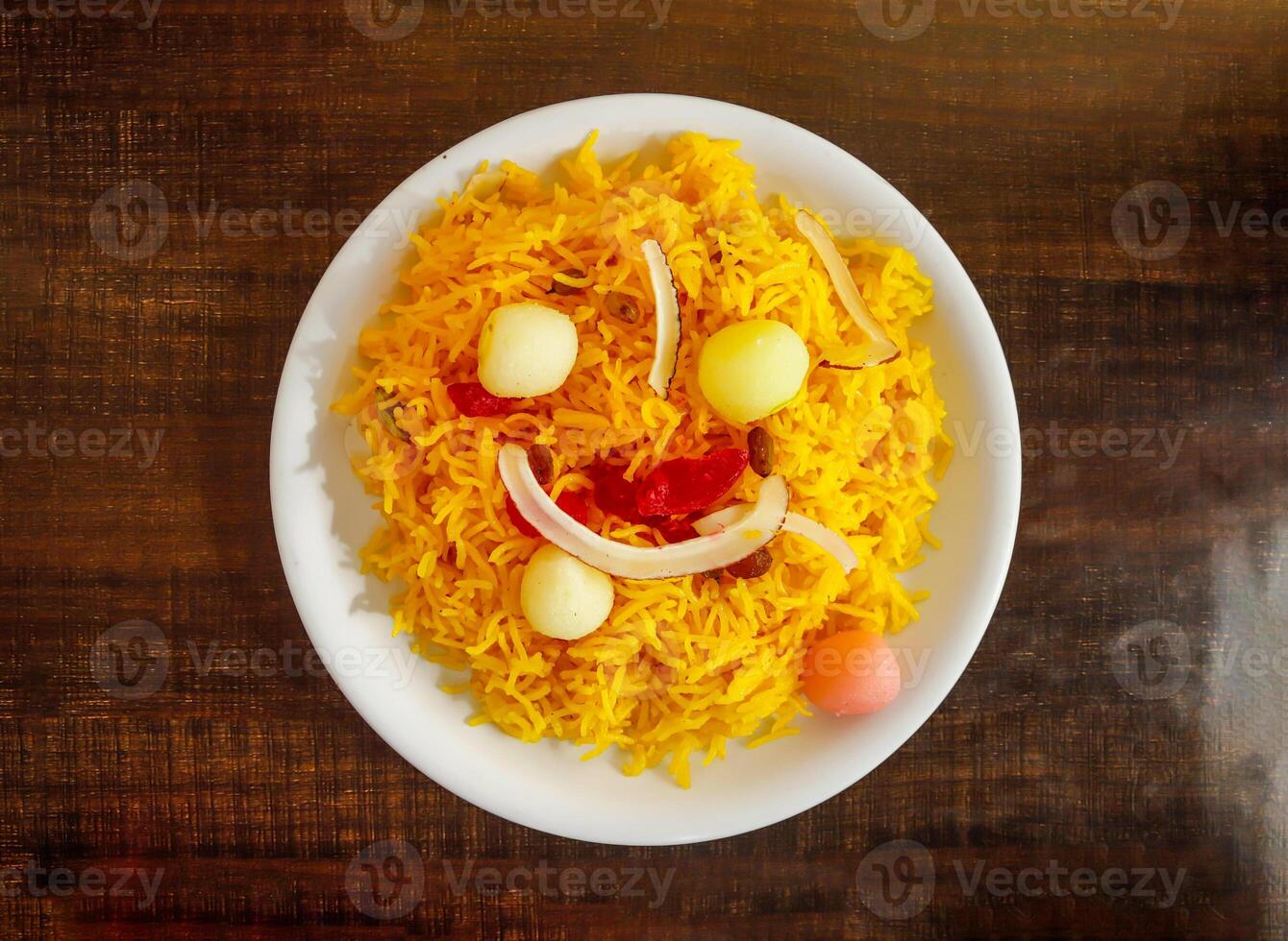Zarda or jorda sweet colorful rice toping with gulab jamun, rasgulla, coconut and Raisins served in plate isolated wooden background top view indian sweet and pakistani dessert food photo