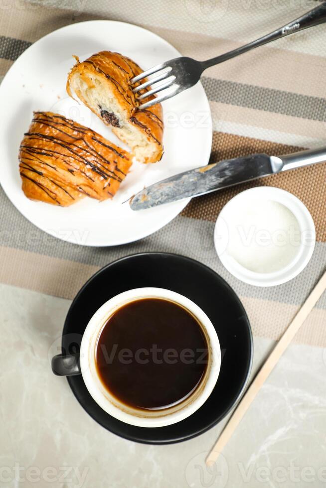 Americano coffee served in cup with croissant, puff pastry, bread and knife isolated on napkin top view cafe breakfast photo