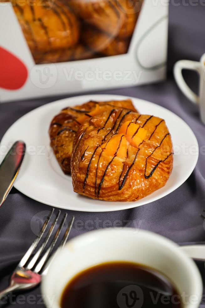 Peach Danish pastry puff served in plate with cup of black coffee isolated on napkin with fork and knife side view of french breakfast baked food item on grey background photo