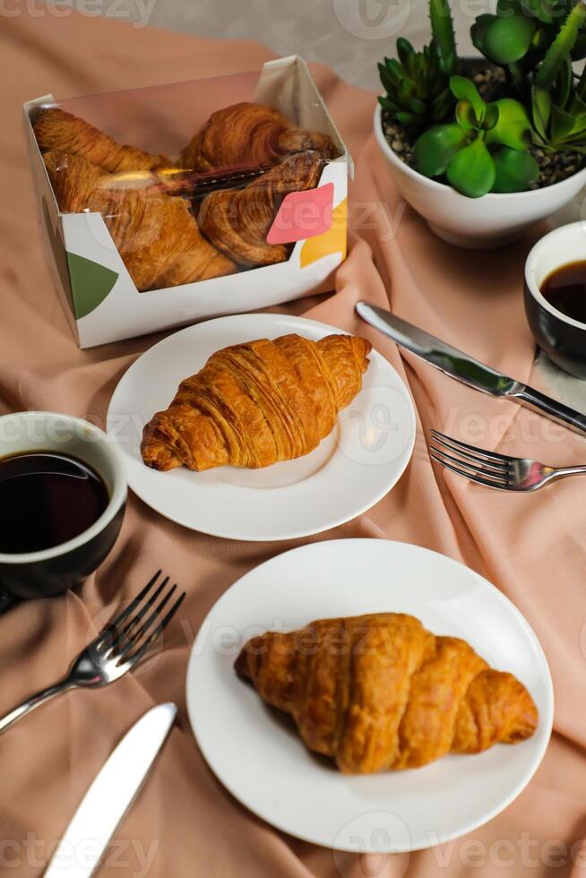 llanura cuerno servido en de madera tablero con taza de negro café aislado en servilleta con cuchillo y tenedor lado ver de francés desayuno horneado comida articulo en gris antecedentes foto