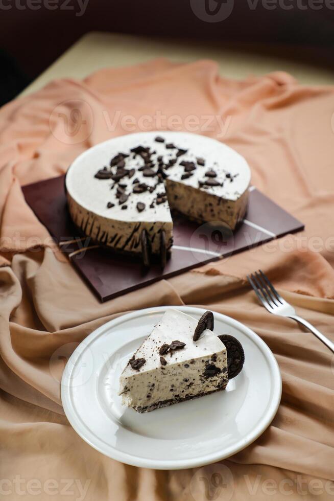 Oreo Cheesecake slice include chocolate, cream, sugar with fork and flowers served in plate isolated on napkin side view of cafe food photo