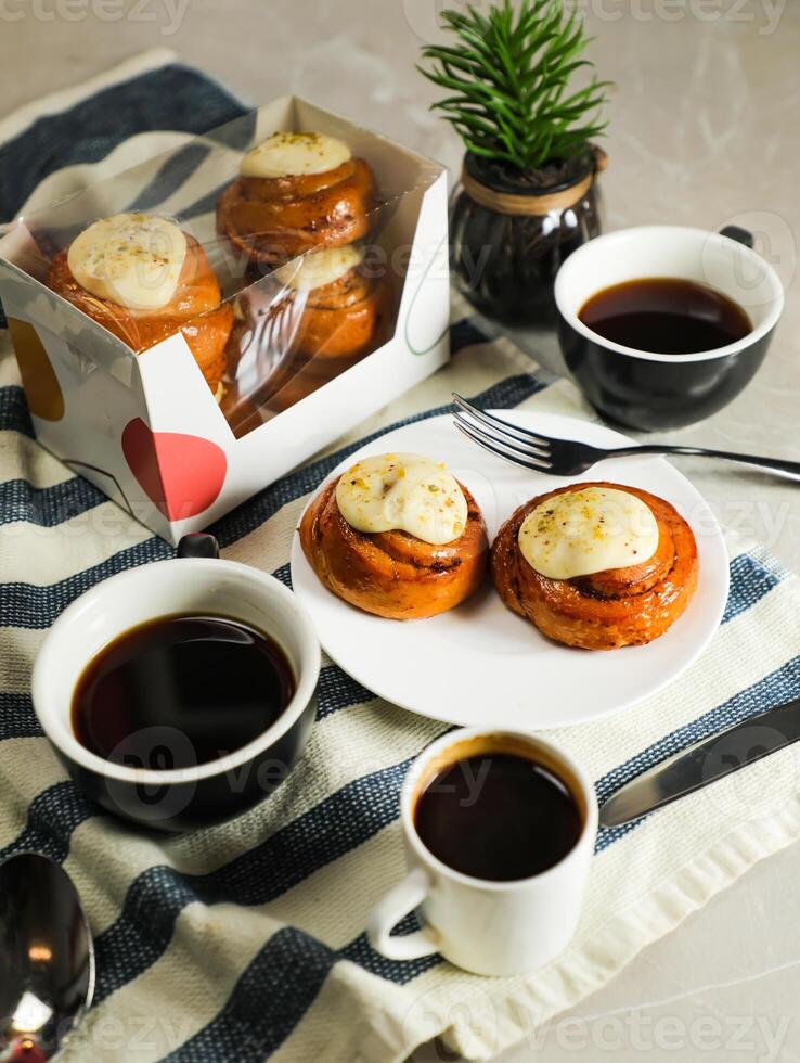 Cinnamon Roll served in plate with cup of black coffee with knife and fork isolated on napkin side view of french breakfast baked food item photo