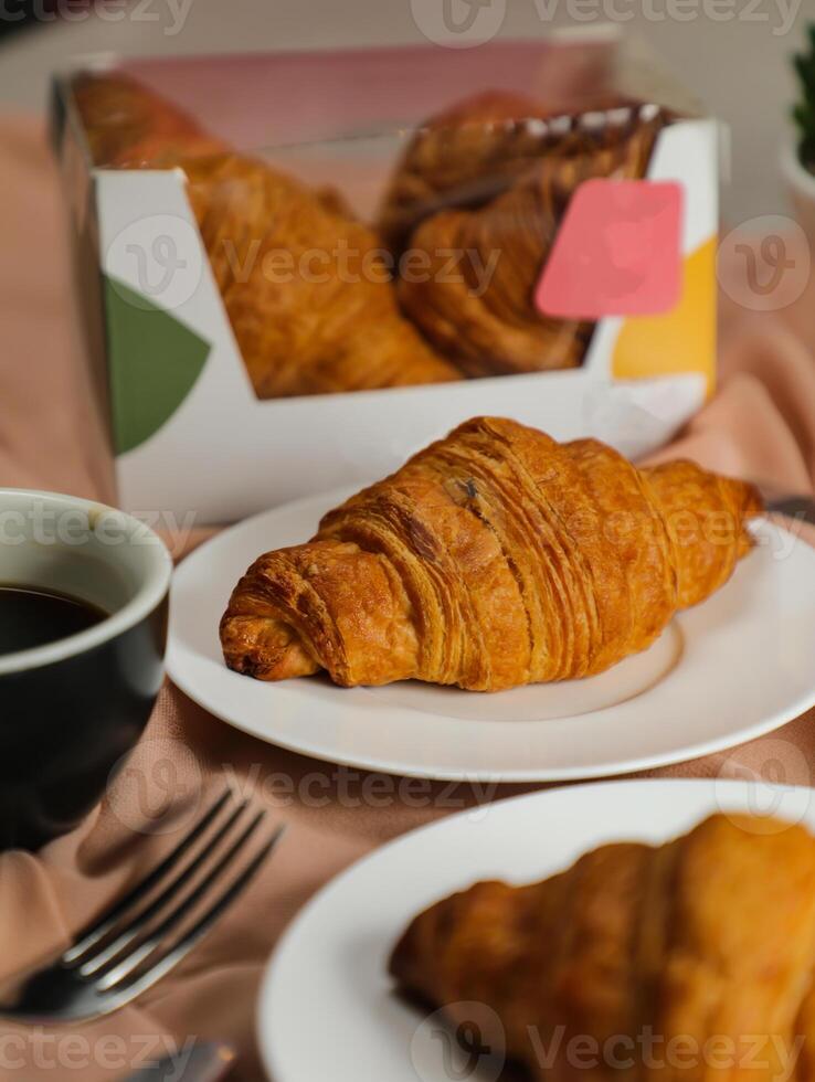 Plain Croissant served on wooden board with cup of black coffee isolated on napkin with knife and fork side view of french breakfast baked food item on grey background photo