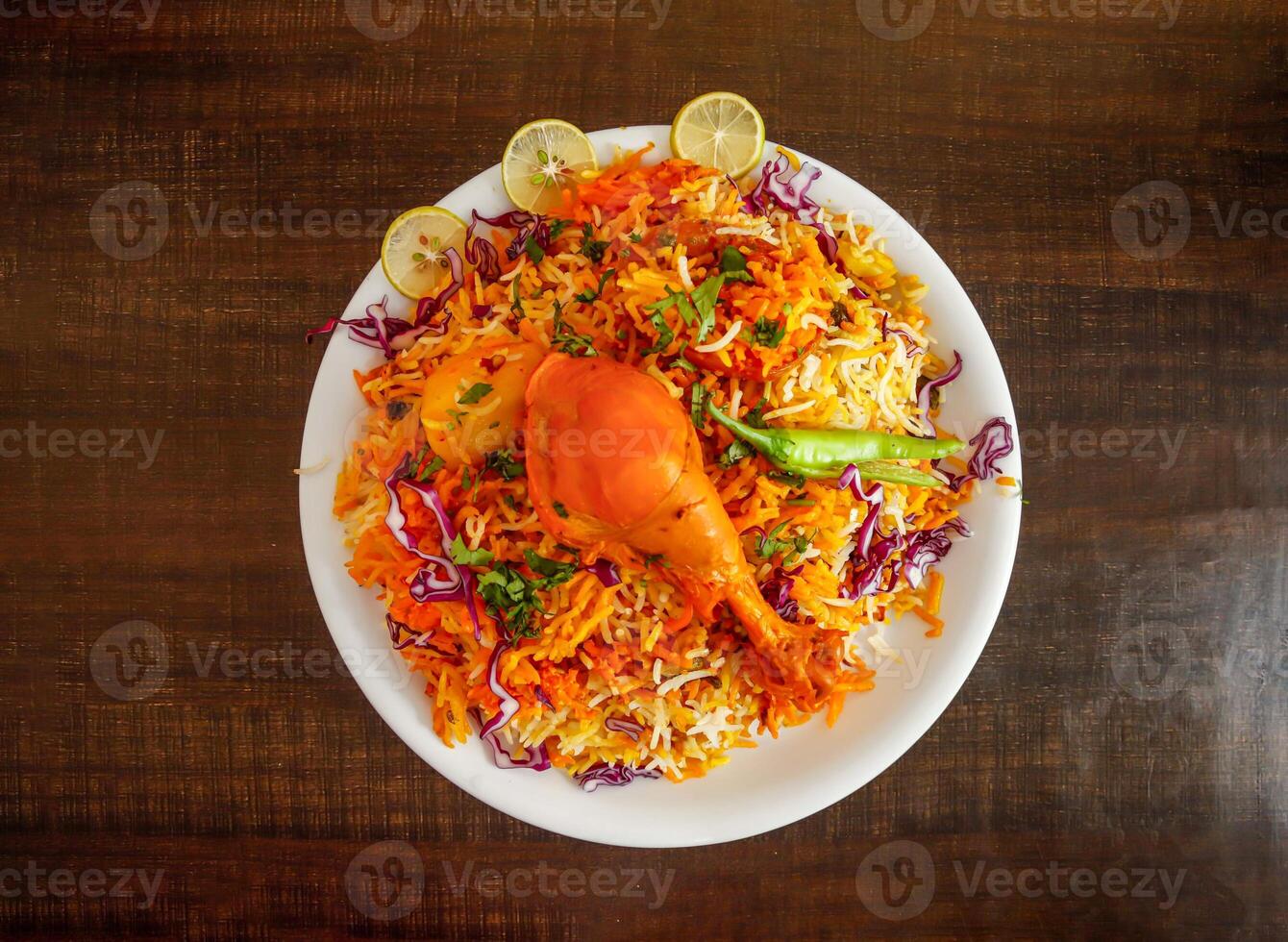 Spicy chicken biryani with potato, onion and lemon slice served in plate isolated wooden background top view indian spices and pakistani food photo