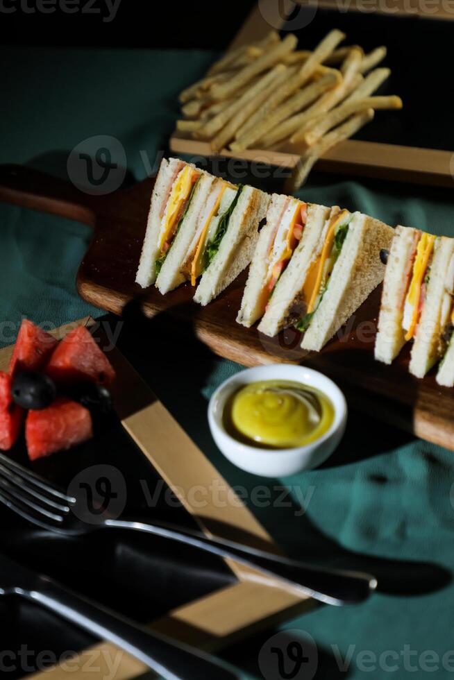 Assorted Club Sandwich isolated on wooden with mayonnaise dip and french fries bucket board side view of italian fast food on background photo