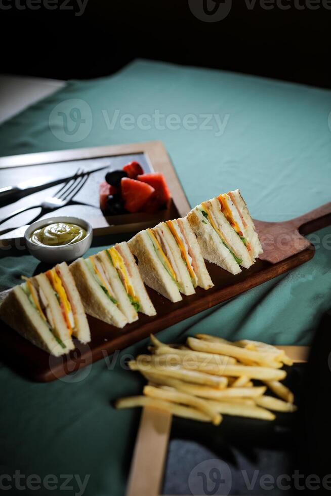 Assorted Club Sandwich isolated on wooden with mayonnaise dip and french fries bucket board side view of italian fast food on background photo