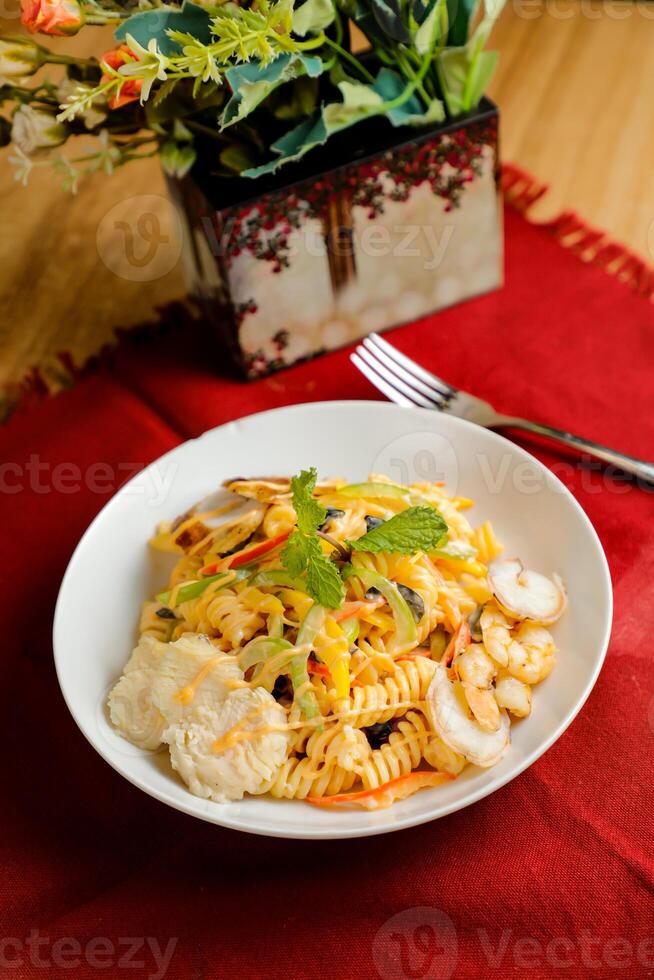 tropical pasta ensalada con mezcla carne aceituna con camarón y gamba servido en cuenco con flores y tenedor aislado en rojo servilleta lado ver de sano verde comida en mesa foto