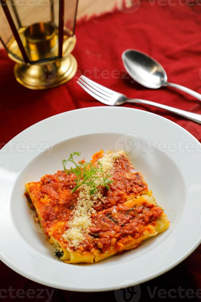 Spicy Tomato and Beef Lasagna served in plate with fork and spoon isolated on red napkin side view of fast food on table photo