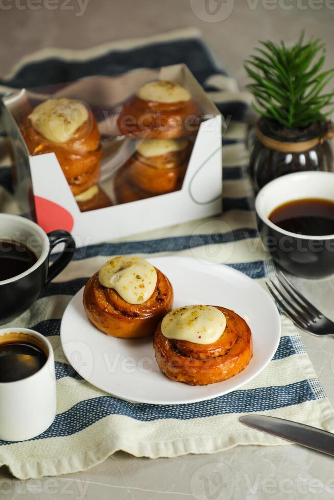 Cinnamon Roll served in plate with cup of black coffee with knife and fork isolated on napkin side view of french breakfast baked food item photo