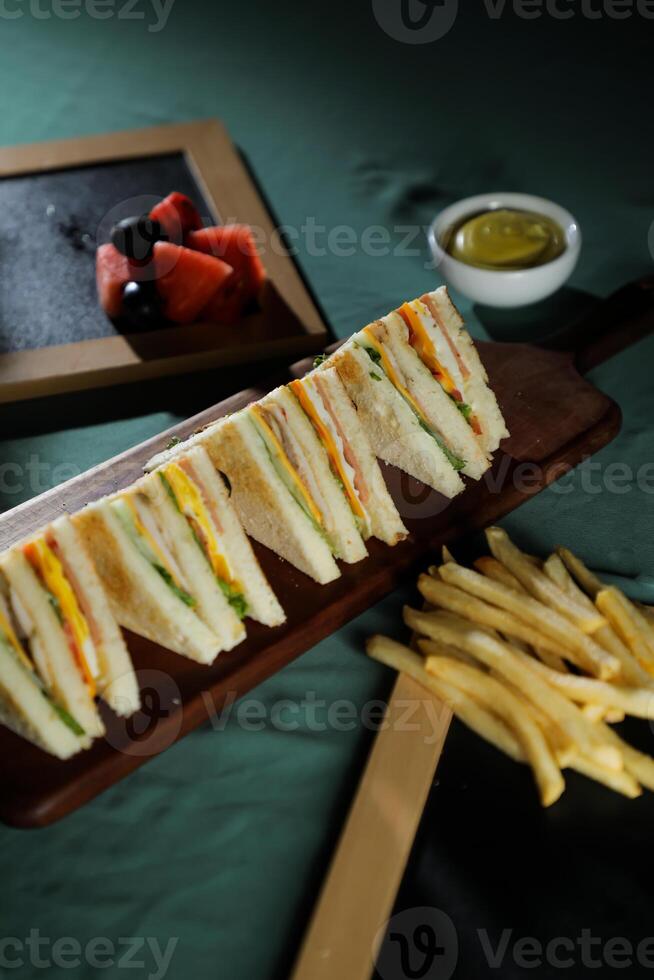 Assorted Club Sandwich isolated on wooden with mayonnaise dip and french fries bucket board side view of italian fast food on background photo