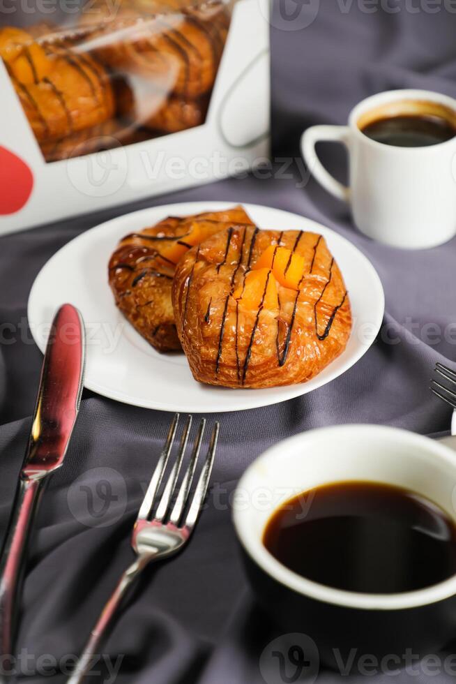 Peach Danish pastry puff served in plate with cup of black coffee isolated on napkin with fork and knife side view of french breakfast baked food item on grey background photo