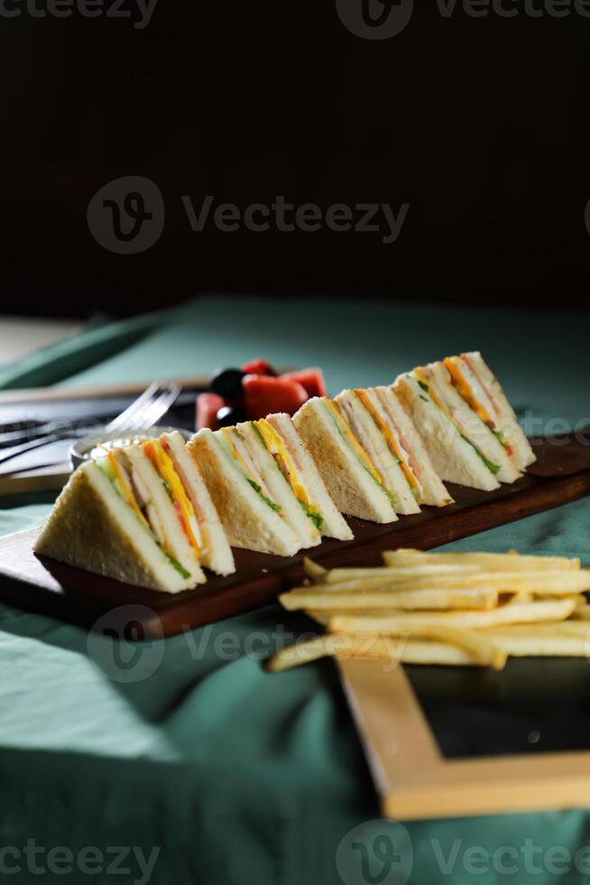 Assorted Club Sandwich isolated on wooden with mayonnaise dip and french fries bucket board side view of italian fast food on background photo
