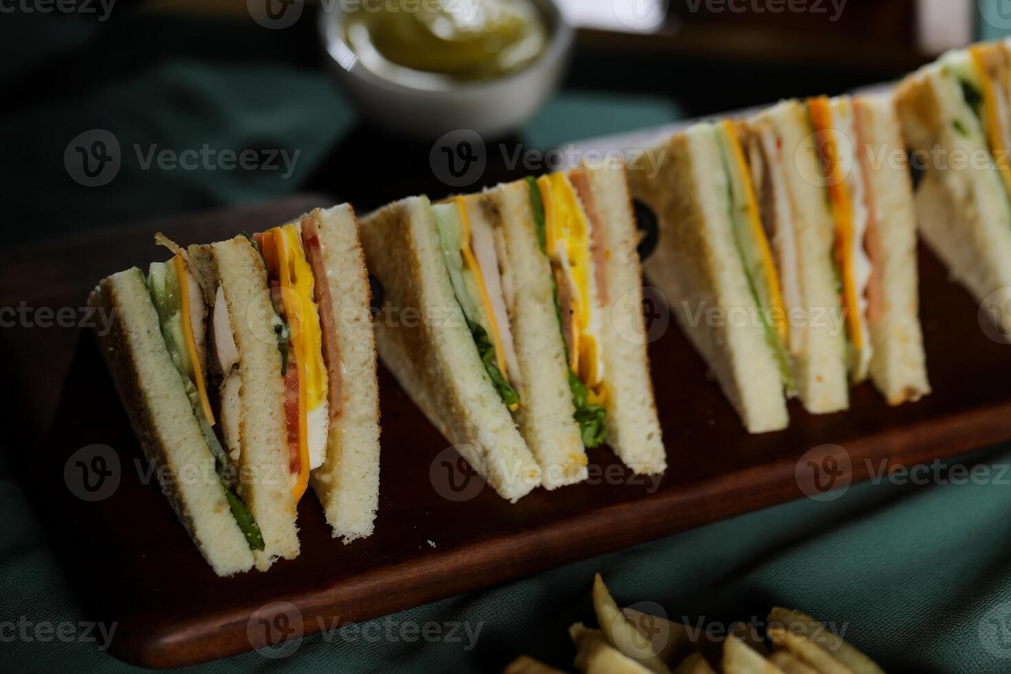 Assorted Club Sandwich isolated on wooden with mayonnaise dip and french fries bucket board side view of italian fast food on background photo