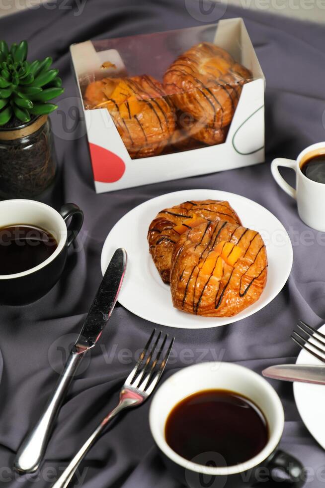 Peach Danish pastry puff served in plate with cup of black coffee isolated on napkin with fork and knife side view of french breakfast baked food item on grey background photo