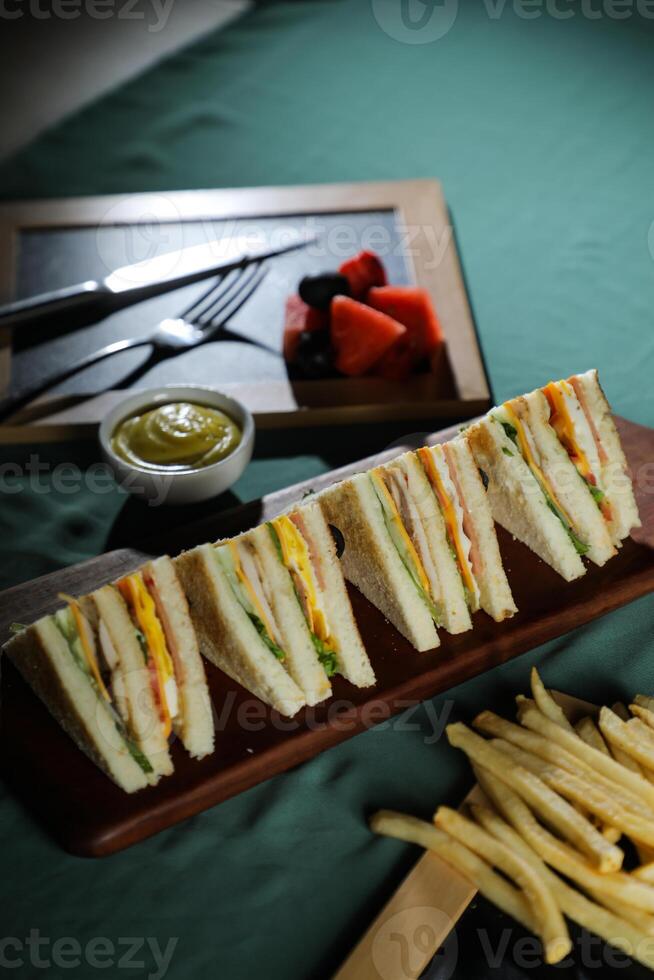 Assorted Club Sandwich isolated on wooden with mayonnaise dip and french fries bucket board side view of italian fast food on background photo