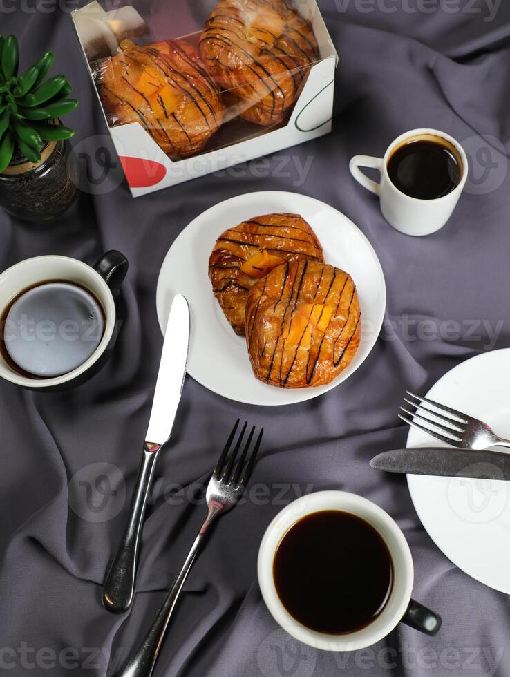 Peach Danish pastry puff served in plate with cup of black coffee isolated on napkin with fork and knife top view of french breakfast baked food item on grey background photo