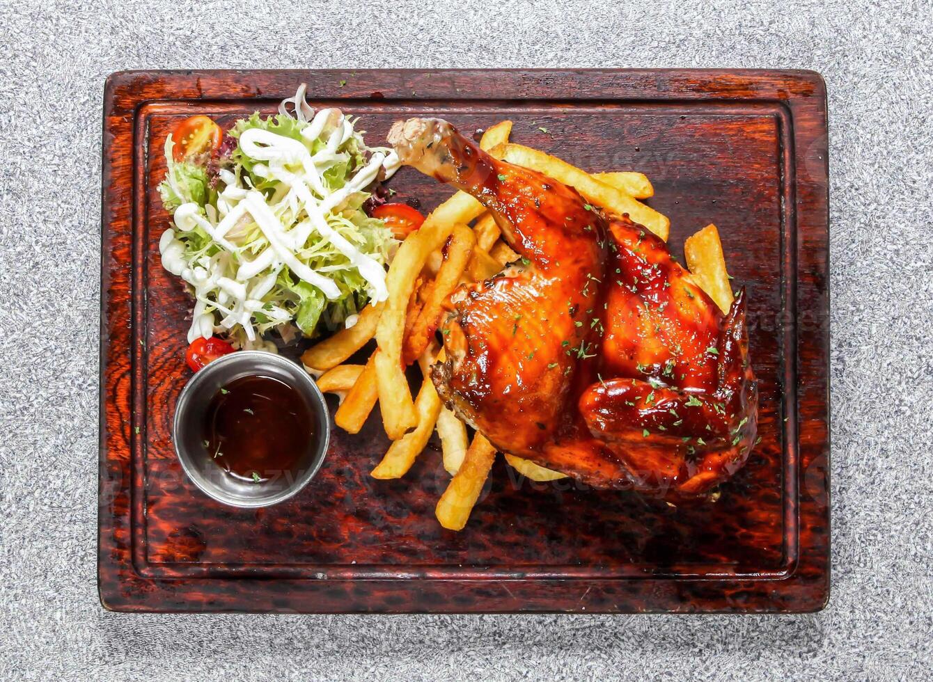bbq spring chicken with fries, salad and sauce served in wooden board isolated on background top view of hong kong food photo