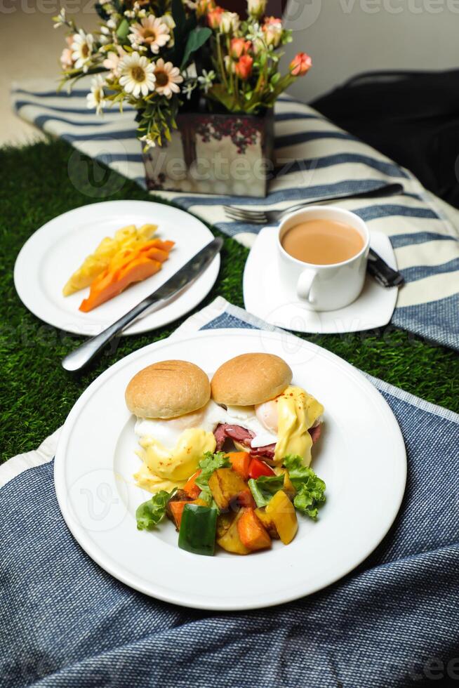 Egg Benedict slider with vegetable salad include tomato, potato, lettuce leaf and carrot with tea, coffee, and sweet melon served on food table top view healthy english breakfast photo