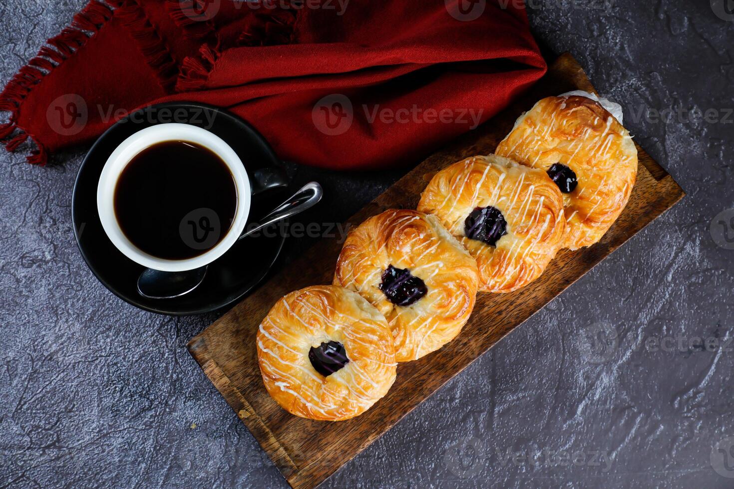 Blueberry Custard Danish served on wooden board with cup of black coffee isolated on napkin top view of french breakfast baked food item on grey background photo