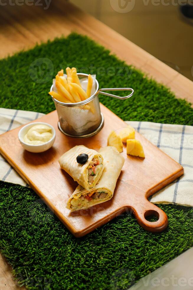 Classic Cajun Beef Double Cheese wrap roll filled with tomato, onion, cucumber with french fries, mayo dip served on wooden board top view of fastfood appetizer photo