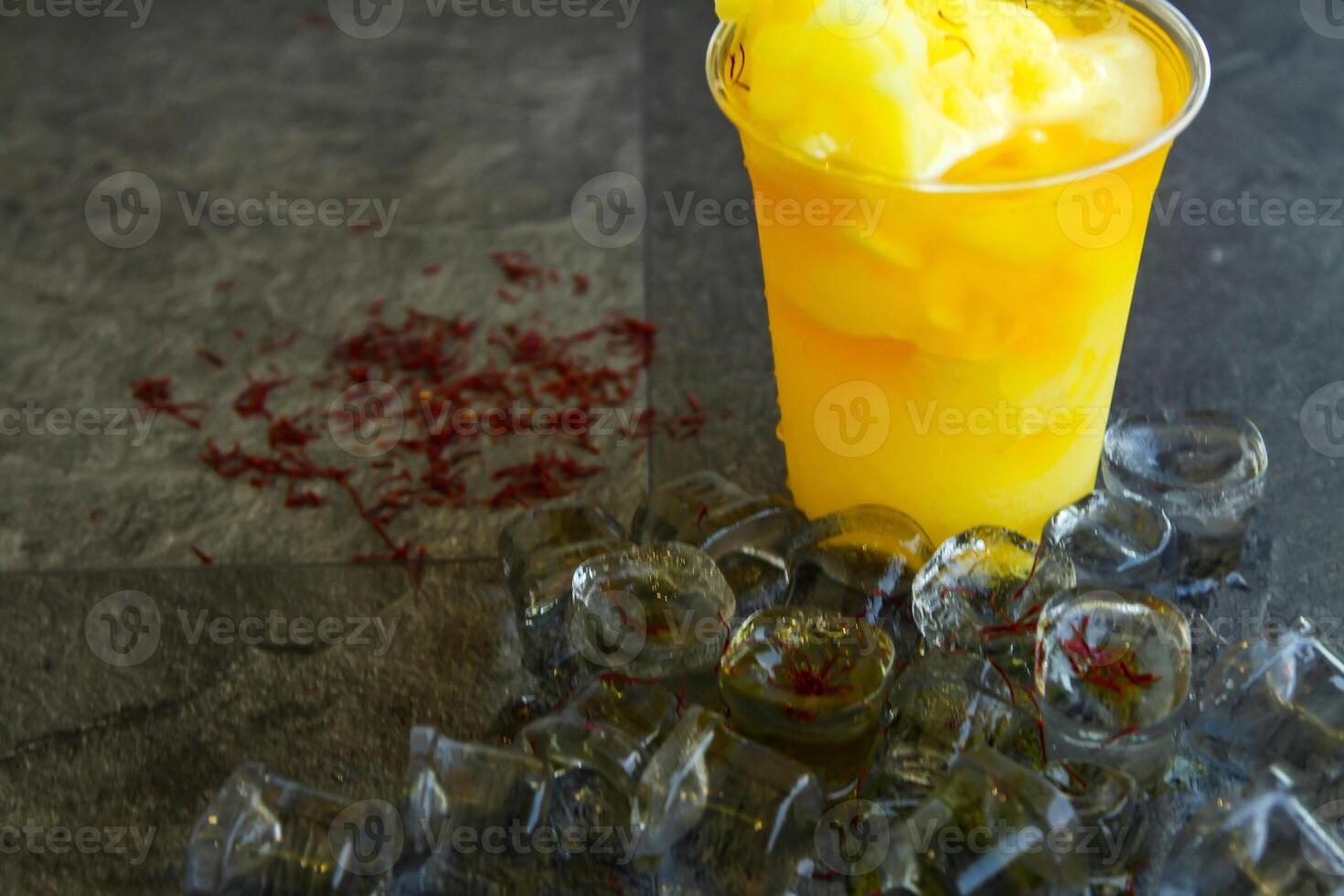 Saffron smoothie with ice cube served in disposable glass isolated on table side view of healthy morning smoothie drink photo