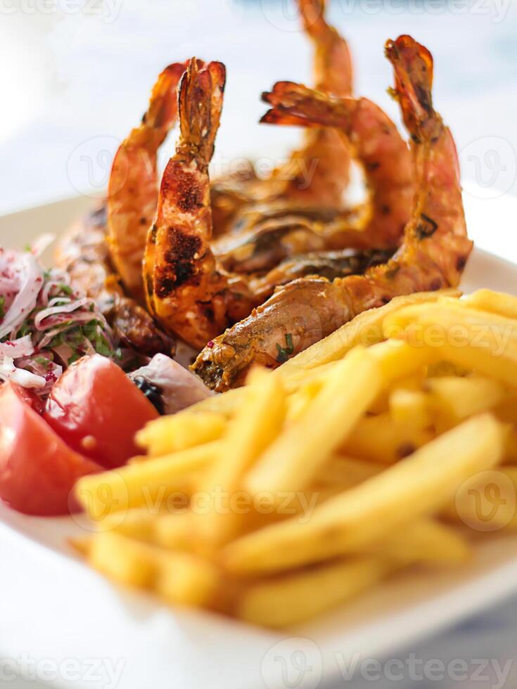GRILLED PRAWNS with french fries, tomato and onion served in dish isolated on table closeup top view of grilled seafood photo