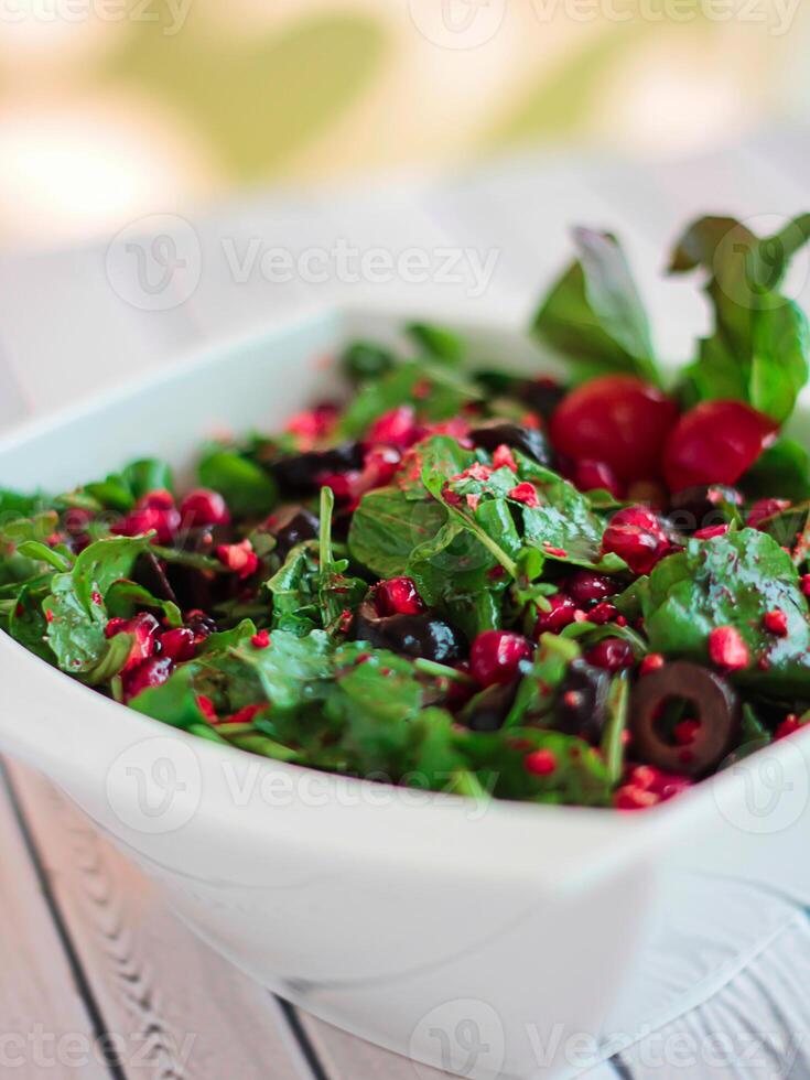 ROCCA SALAD SOUR with pomegranate seeds, olives and herbs leaves served in dish isolated on table closeup top view of healthy organic food photo