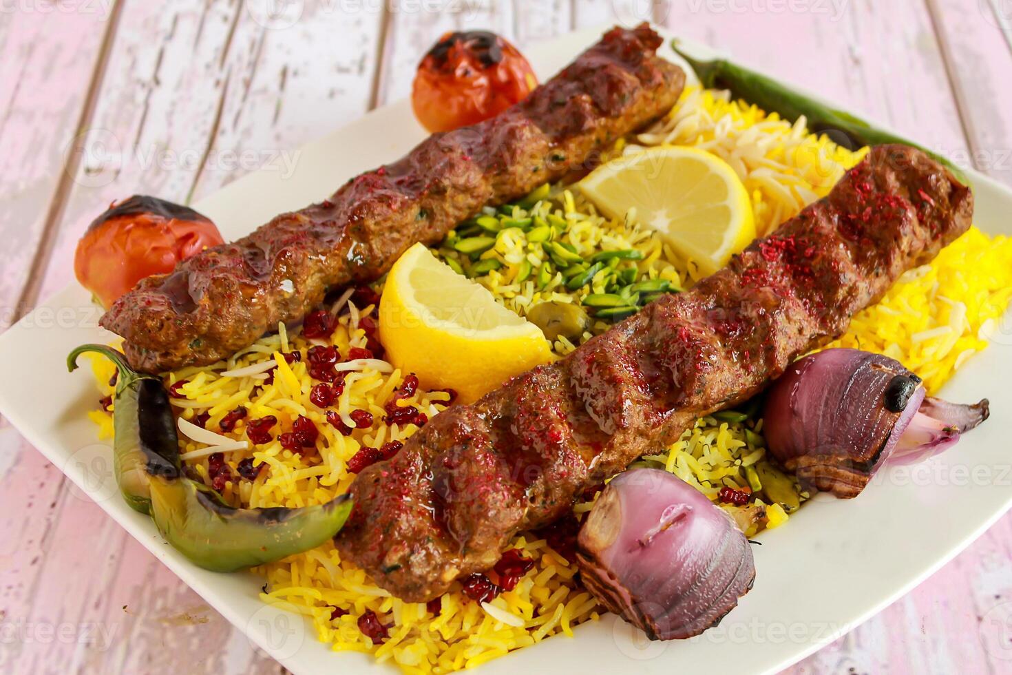 Chelo Kabab Rice topping with pistachio, onion, tomato, lemon slice and pomegranate seeds served in dish isolated on table closeup top vie of arabic spicy food photo