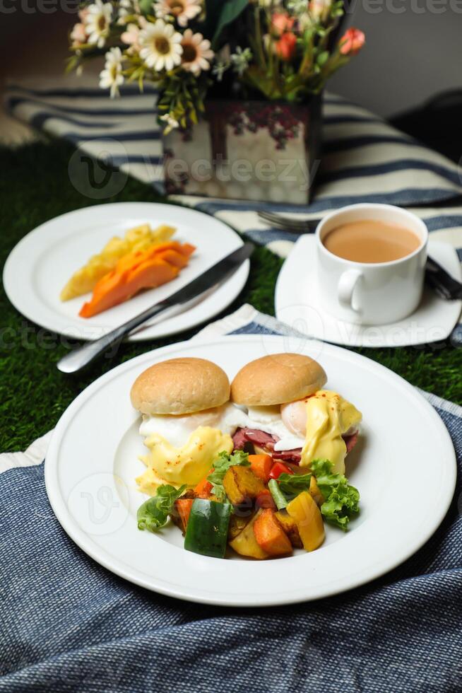 Egg Benedict slider with vegetable salad include tomato, potato, lettuce leaf and carrot with tea, coffee, and sweet melon served on food table top view healthy english breakfast photo