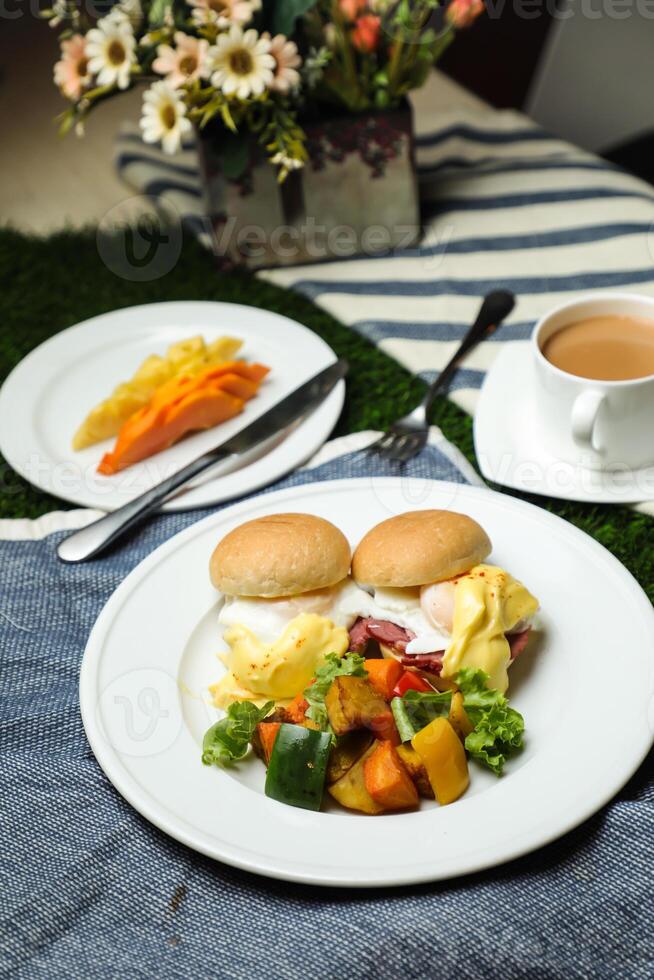 Egg Benedict slider with vegetable salad include tomato, potato, lettuce leaf and carrot with tea, coffee, and sweet melon served on food table top view healthy english breakfast photo