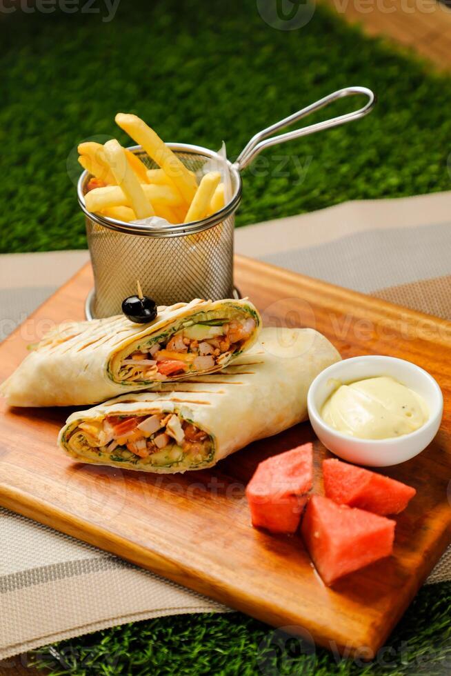 Smoky Chicken Egg Cheese wrap roll filled with tomato, onion, cucumber, with french fries, mayo dip and watermelon slice served on wooden board top view of fastfood appetizer photo
