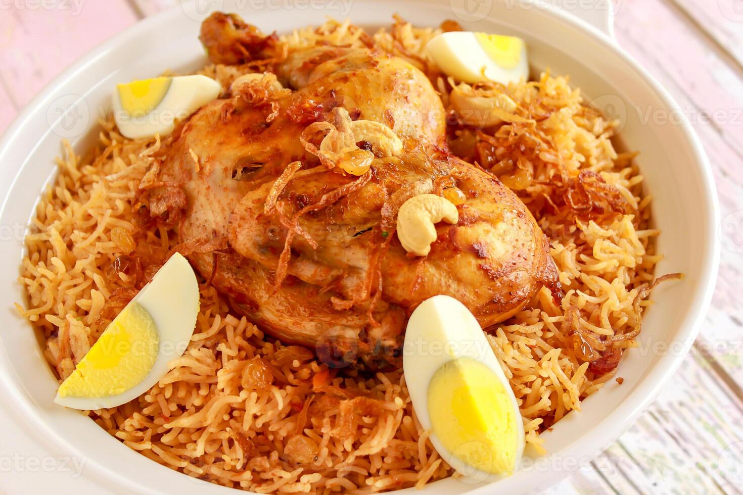 Saudi Chicken Kabsa pulao rice with fried onion, cashew nut and boiled egg served in pot dish isolated on wooden table top view arabic spicy food photo