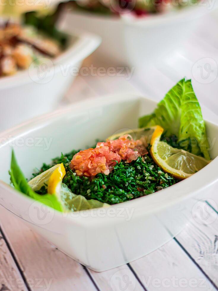TABOULEH Salad with tomato, green herb leaves and lemon served in dish isolated on wooden table top view of cold mazza arabic food photo