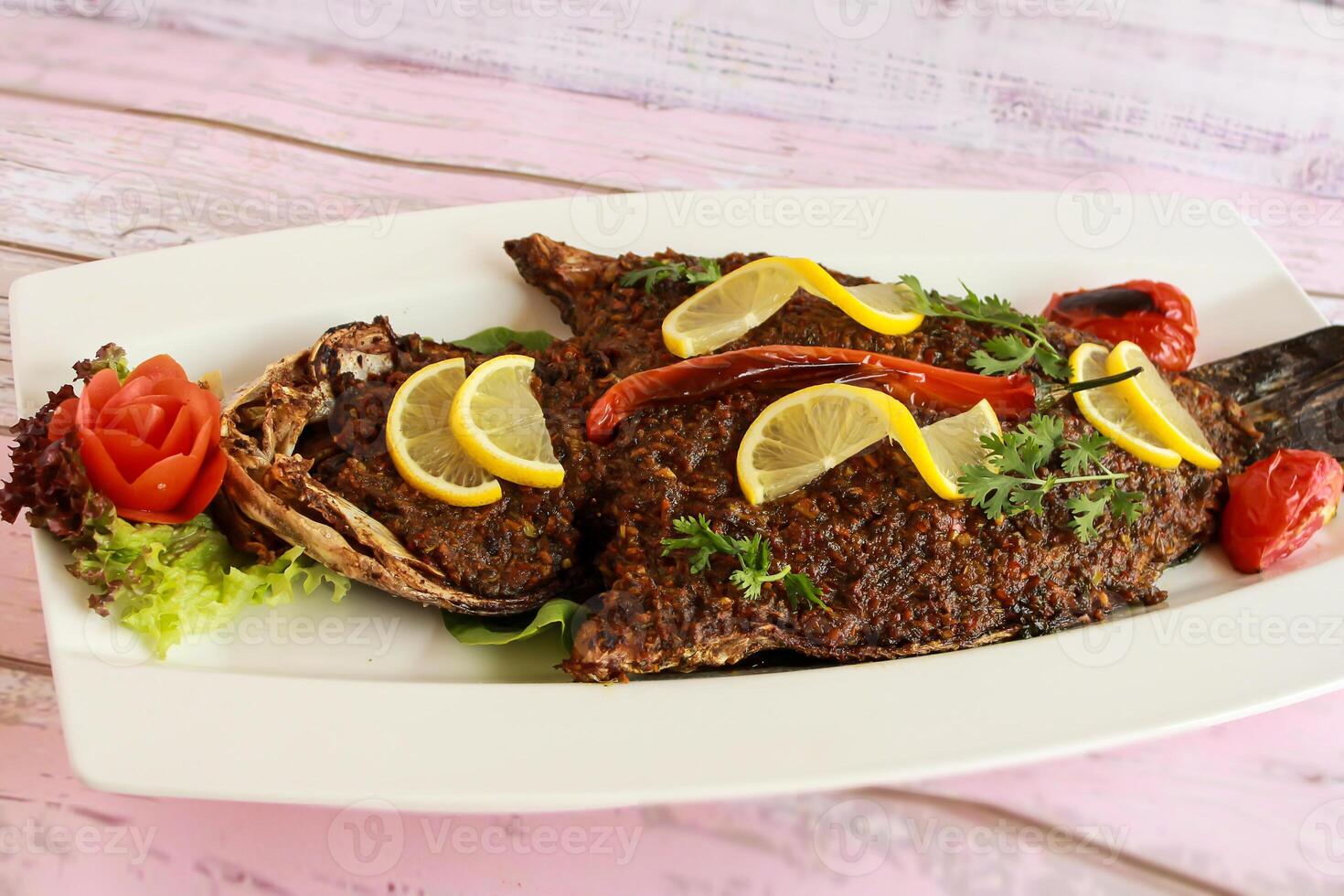 GRILLED SEA BASS Fish with lemon slice and tomato served in dish isolated on table closeup top view of grilled seafood photo