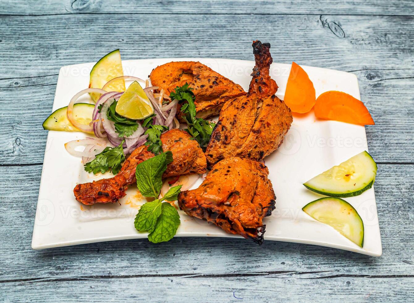 Grilled tandoori chicken with lemon and onion served in dish isolated on wooden table top view of indian spicy food photo