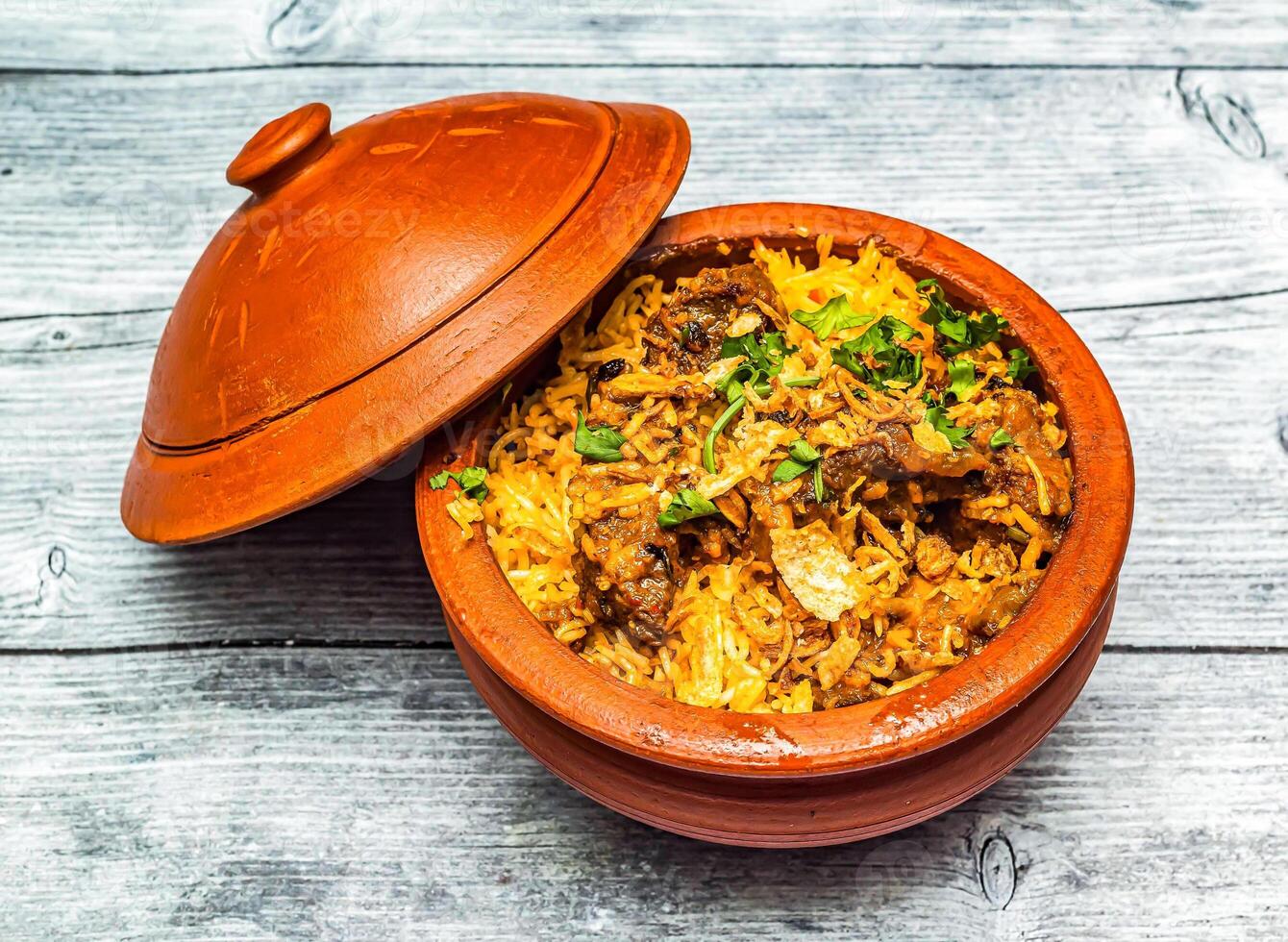 Hyderabadi mutton biryani served in claypot dish isolated on wooden table top view of indian spicy food photo