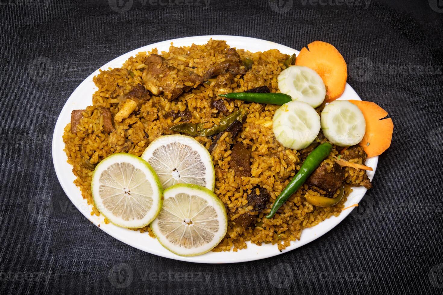 Beef Yakhni biryani rice pulao with cucumber, lime slice and carrot served in dish isolated on dark background top view indian spices, bangladeshi and pakistani food photo