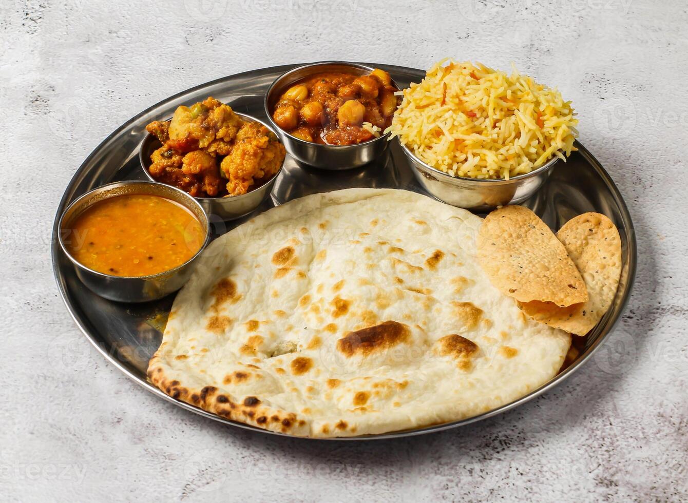 Vegetable thali set with plain biryani, mixed vegetable of aloo gobi matar, chanay, shorba and chapati served in dish isolated on background top view of indian spicy food photo