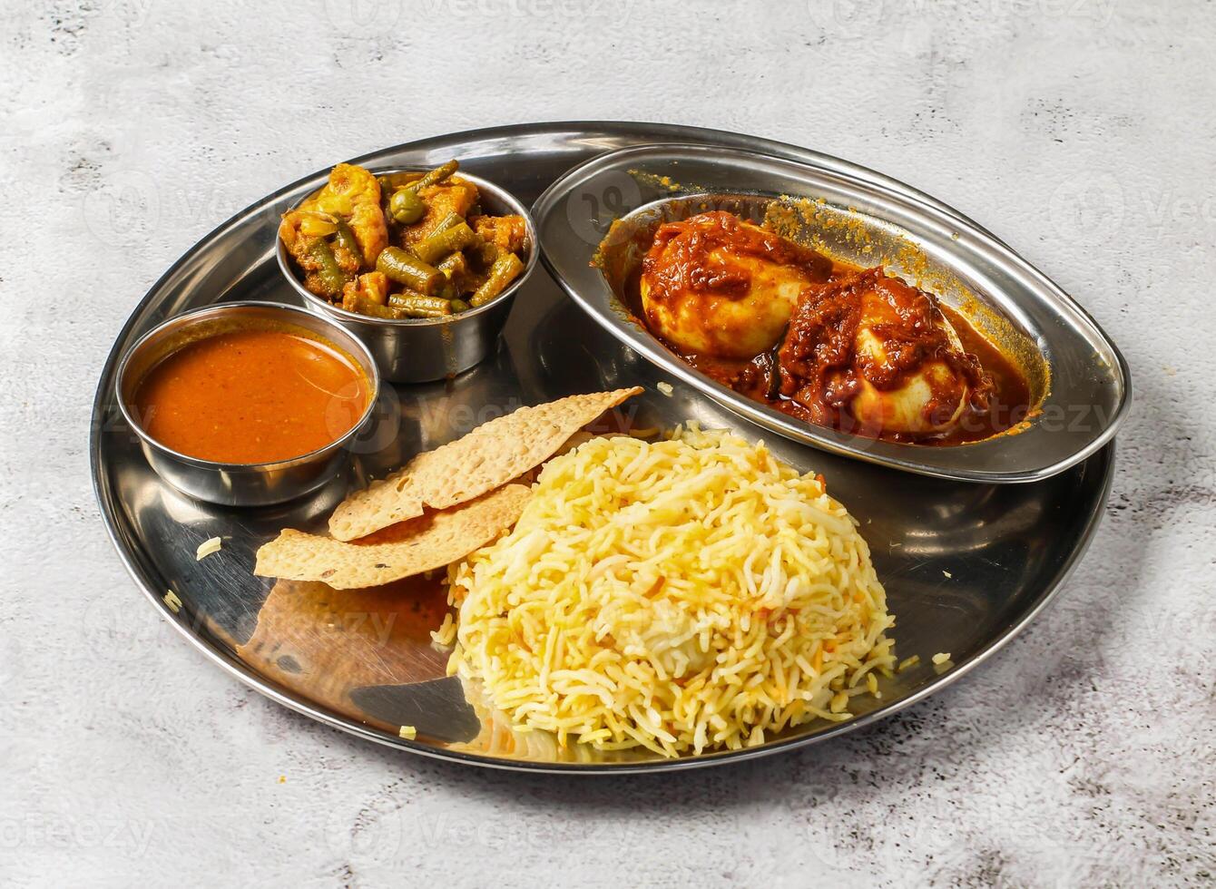 Boiled egg biryani thali set with gravy, mixed vegetable of aloo gobi matar, nachos and shorba served in dish isolated on background top view of indian spicy food photo