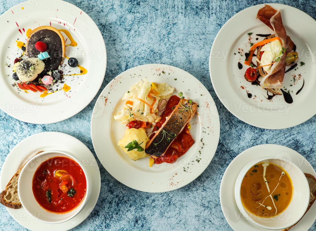 grilled salmon, bruschetta sandwich, tomato soup, pumpkin soup, bread and baked chocolate tart served in plate isolated on background top view of italian food photo