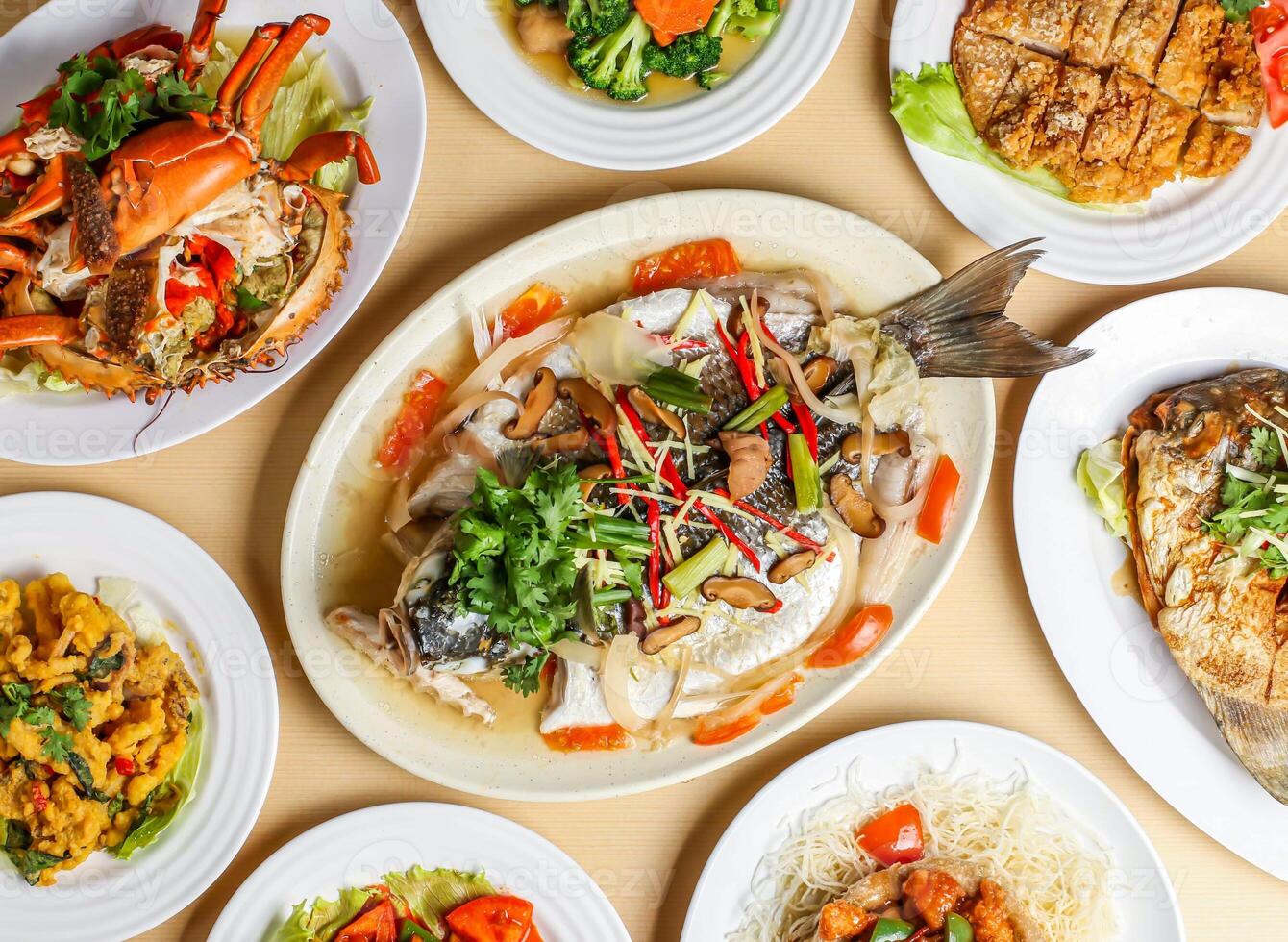 steamed black mullet fish, steamed crab, stir fried broccoli wuth mushroom, fragrant fried chicken, salted egg squid, teochew pomfret, sweet sour and pork yamring top view singapore sea food variety photo