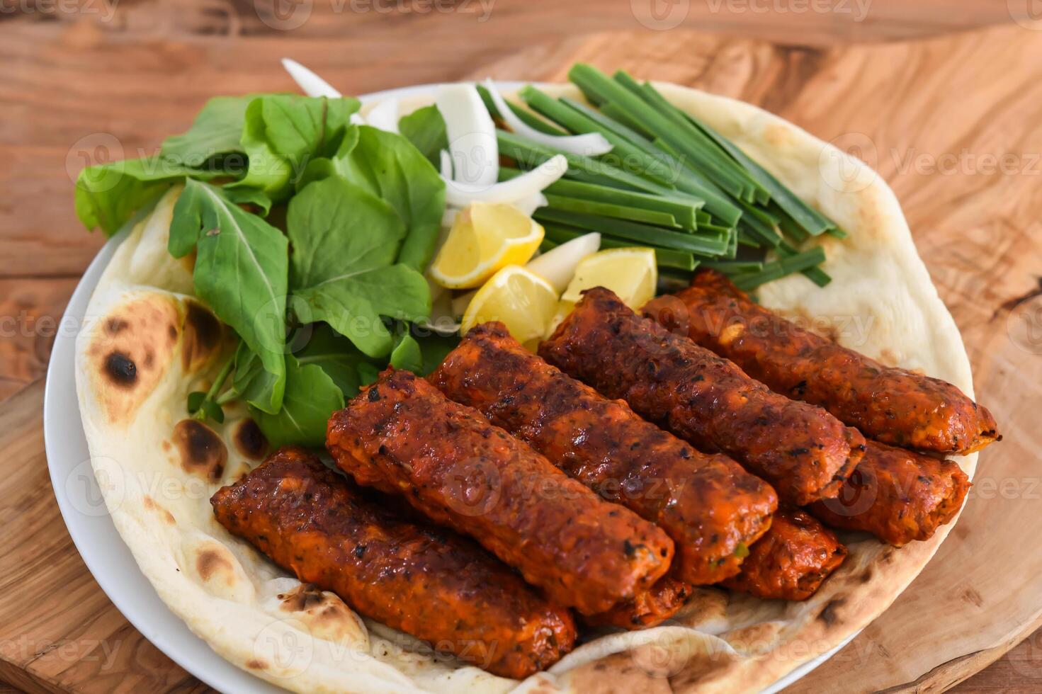 Spicy Chicken kabab meat seekh kebab with bahraini bread tandoori nan, lime and salad served in dish isolated on wooden table top view middle eastern grills food photo