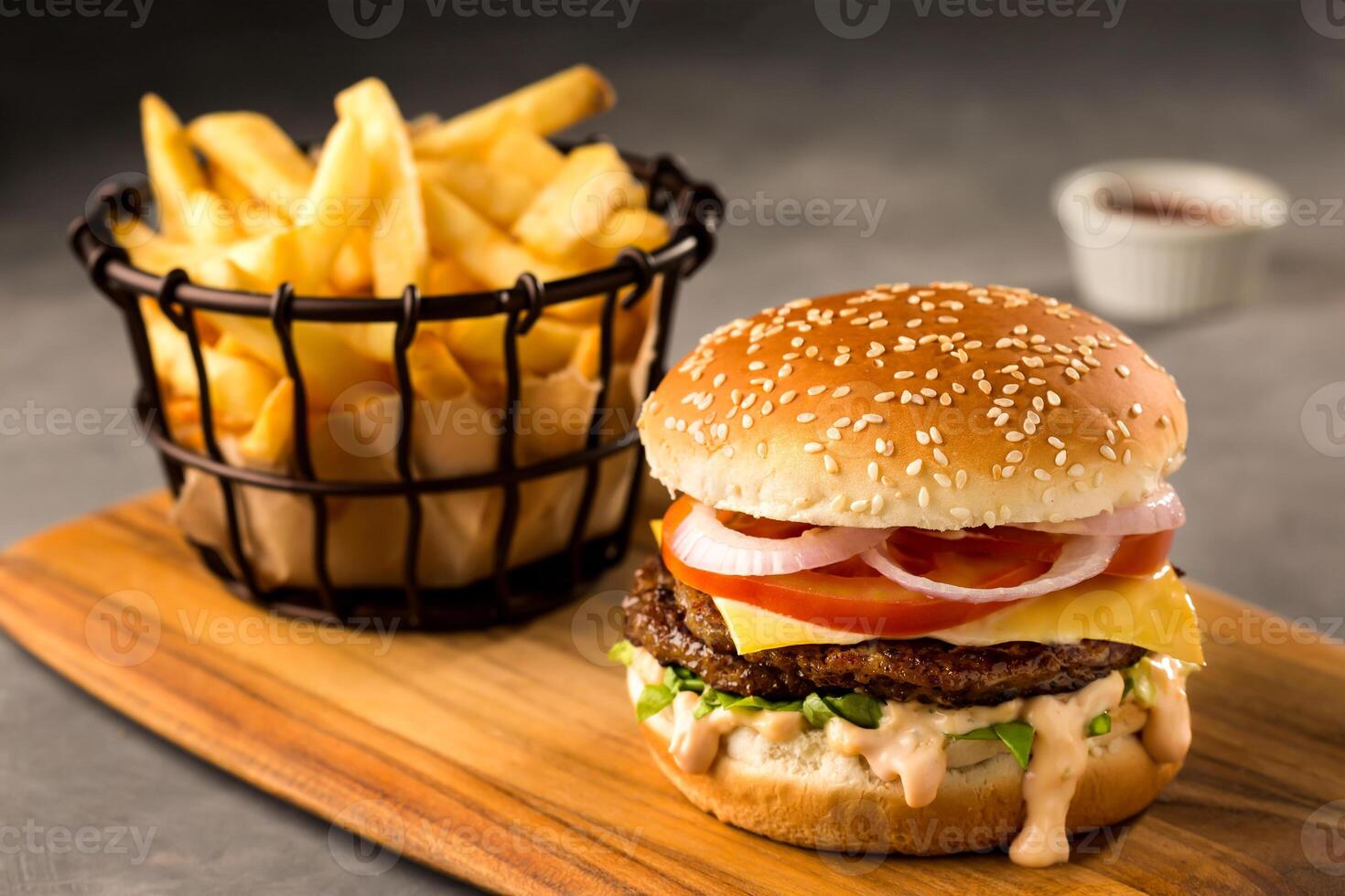 Fresh Spicy Beef Burger with french fries bucket, sesame seeds, tomato, onion, cheese slice, mayonnaise and ketchup served on wooden board top view of junk fast food photo