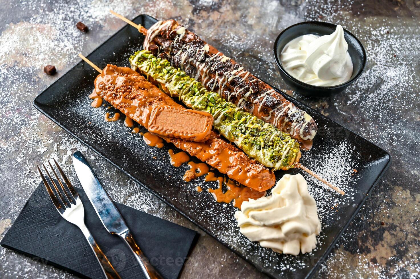 Assorted waffle sticks with Nutella, Oreo, Lotus, Brownie, Pistachio, Chocolate, Whipped cream, knife and fork served in dish isolated on dark background top view cafe dessert food photo