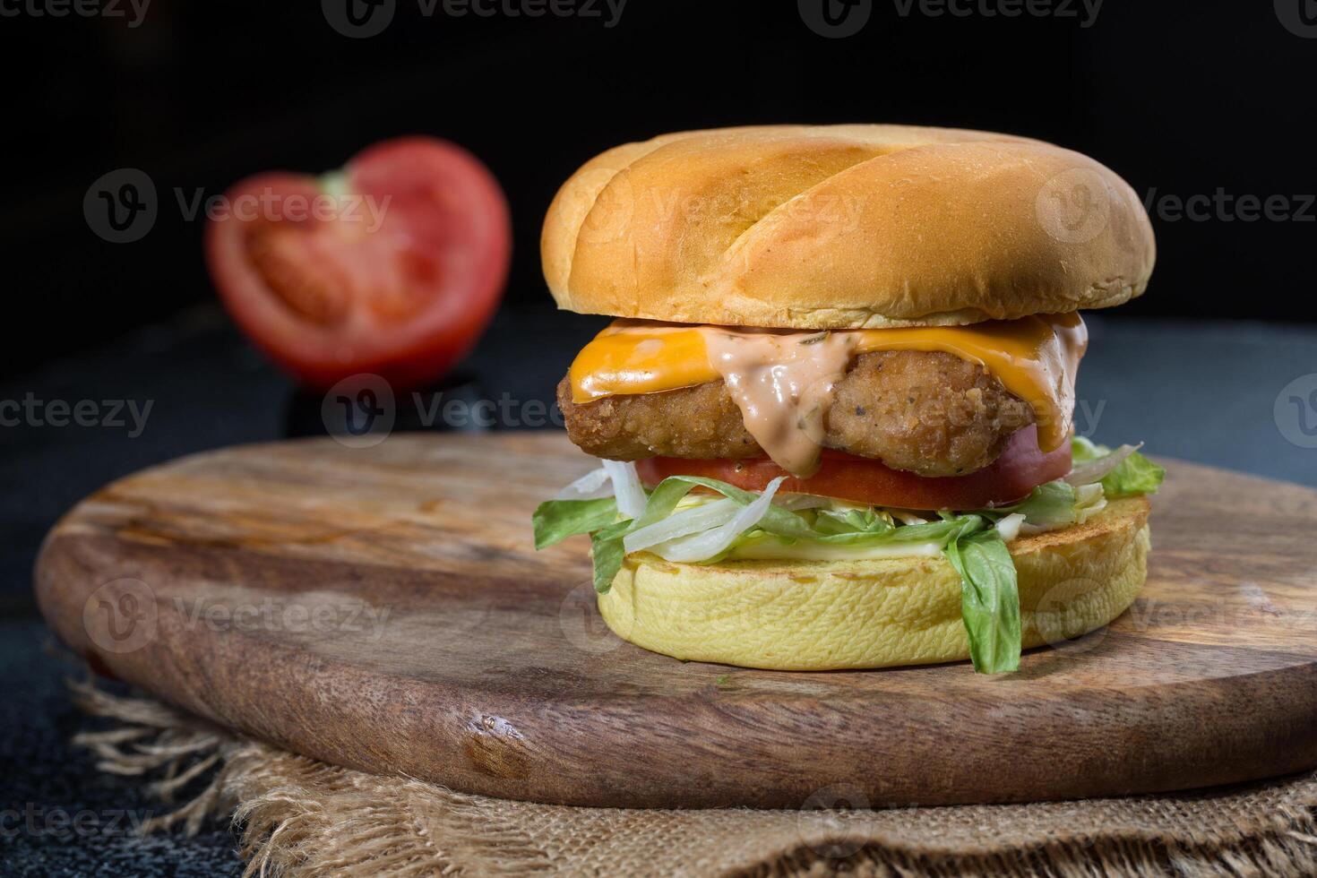 Crispy Chicken Sandwich or burger with cabbage, tomato, lettuce leaf, melted cheese and mayonnaise isolated on wooden board with dip sauce top view of grill food on dark grey background photo